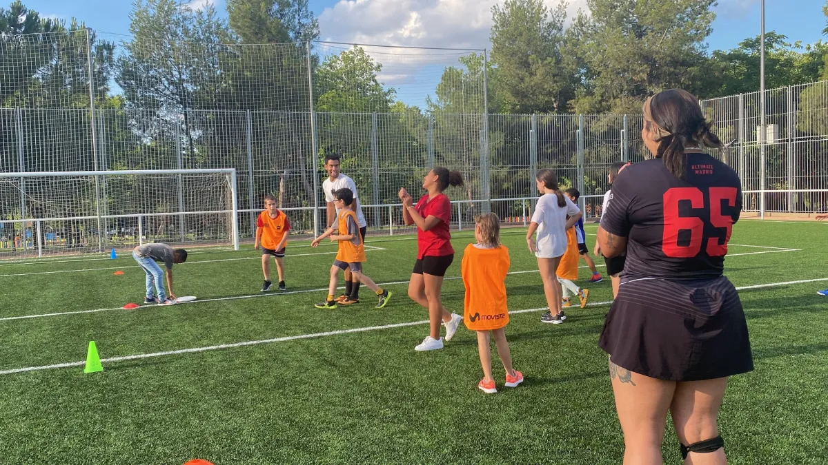 Profesor de educación física enseñando Ultimate Frisbee a alumnos en el patio de un colegio de Madrid